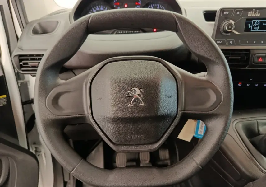 Vue rapprochée du volant noir de la Peugeot Partner 2022, avec tableau de bord et console centrale visibles en arrière-plan.