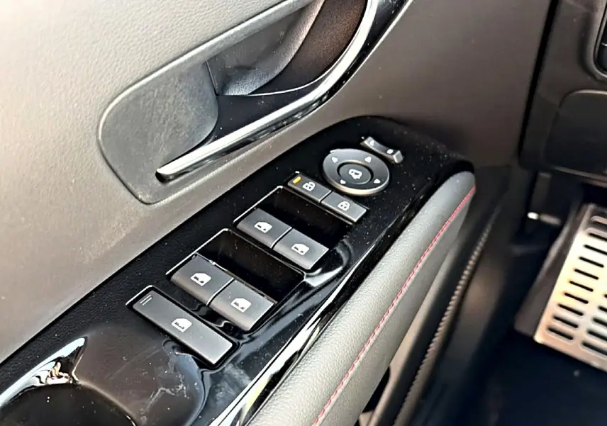Gros plan sur la commande des vitres côté conducteur du Hyundai Tucson gris shadow, avec surpiqûres rouges et poignée chromée.