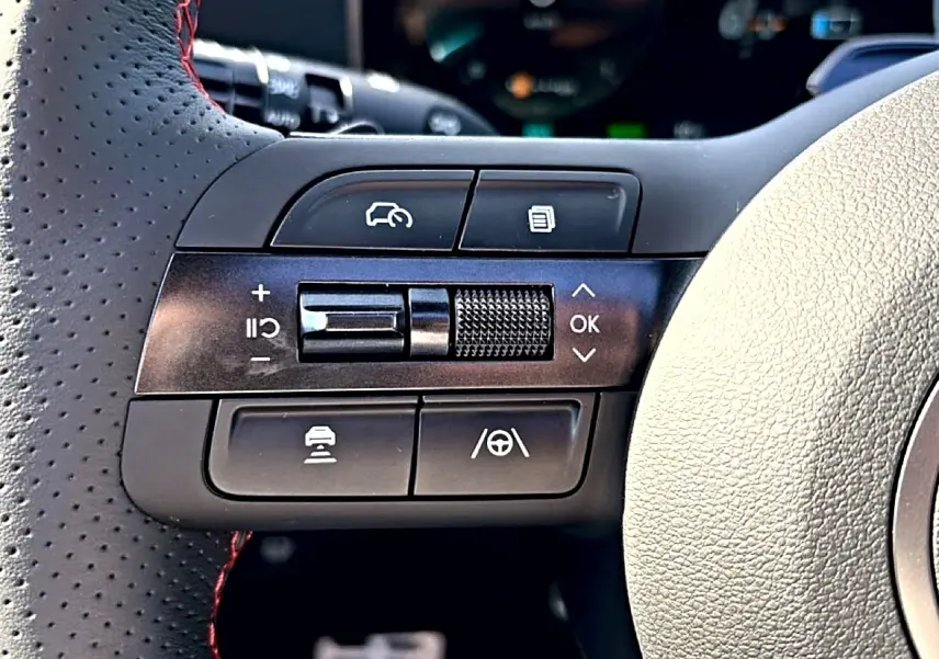 Gros plan sur les commandes noires à gauche du volant cuir perforé avec surpiqûres rouges du Hyundai Tucson gris shadow 2026.