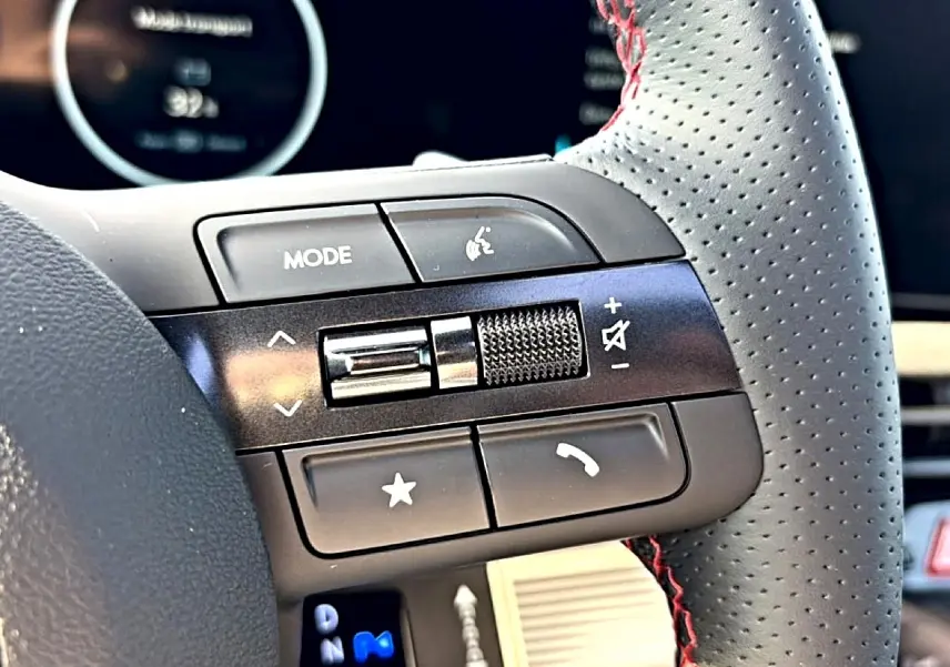 Gros plan sur les commandes gauche du volant cuir perforé gris avec surpiqûres rouges du Hyundai Tucson 2026.