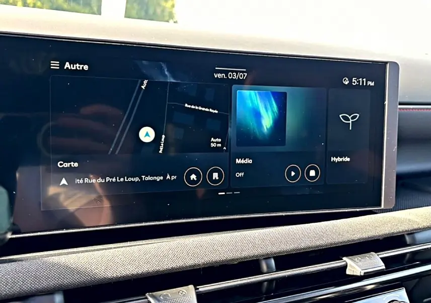 Écran tactile central du Hyundai Tucson 2026 affichant navigation, média et mode hybride, avec tableau de bord gris et détails rouges.