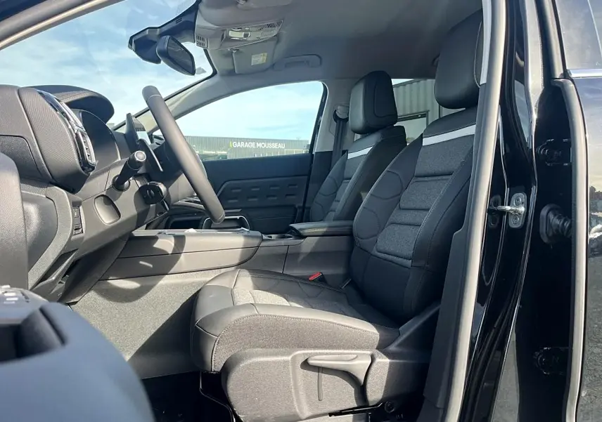 Vue intérieure côté conducteur du Citroën C5 Aircross noir 2025, sièges tissu et cuir noir avec console centrale visible.