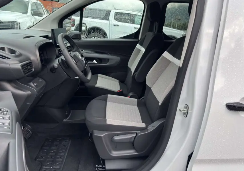 Vue intérieure côté conducteur du Citroën Berlingo Kaolin white 2026, sièges tissu bicolores et volant multifonctions cuir.