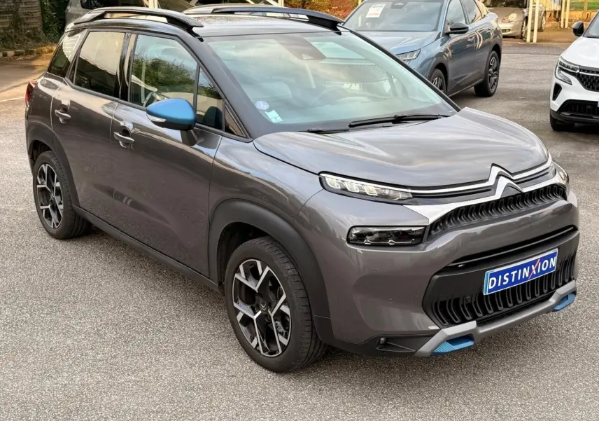 Citroën C3 Aircross gris platinium vue 3/4 avant droit avec rétroviseur bleu et détails bleus sur le pare-chocs.