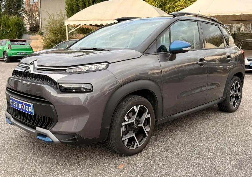 Vue 3/4 avant droit d'un Citroën C3 Aircross gris platinium avec rétroviseurs bleus et jantes noires à motifs géométriques.