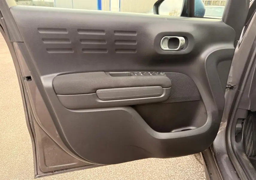 Vue intérieure de la porte avant gauche d'une Citroën C3 Aircross gris platinium avec commandes de vitres et poignée intégrée.