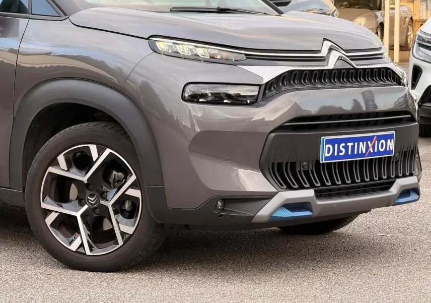 Vue 3/4 avant gauche d'un Citroën C3 Aircross gris platinium avec calandre noire et détails bleus sur le pare-chocs.