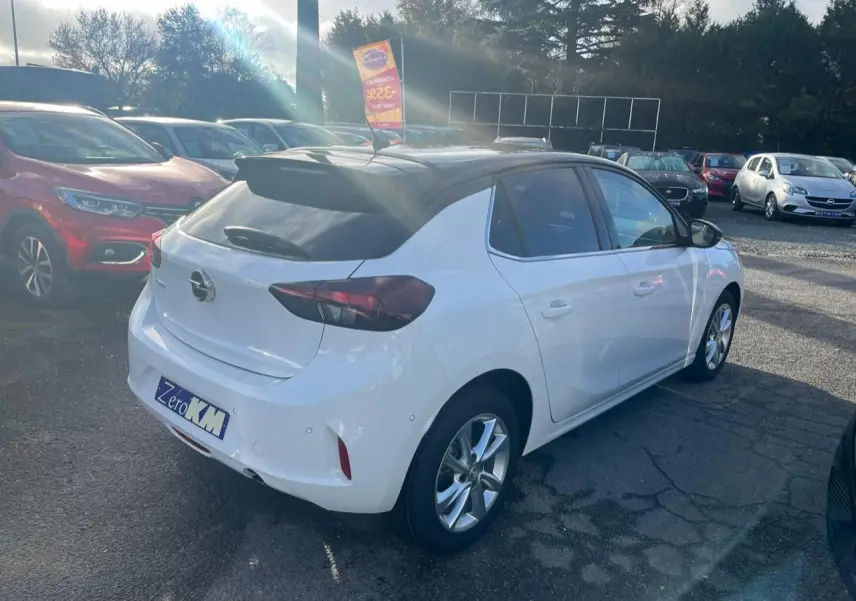 Opel Corsa blanche vue 3/4 arrière droit avec toit noir et feux arrière fumés sur parking extérieur.