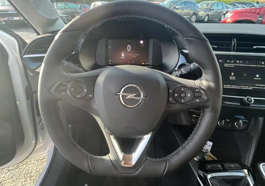 Vue intérieure centrée sur le volant noir de l'Opel Corsa blanc avec tableau de bord digital et écran tactile.