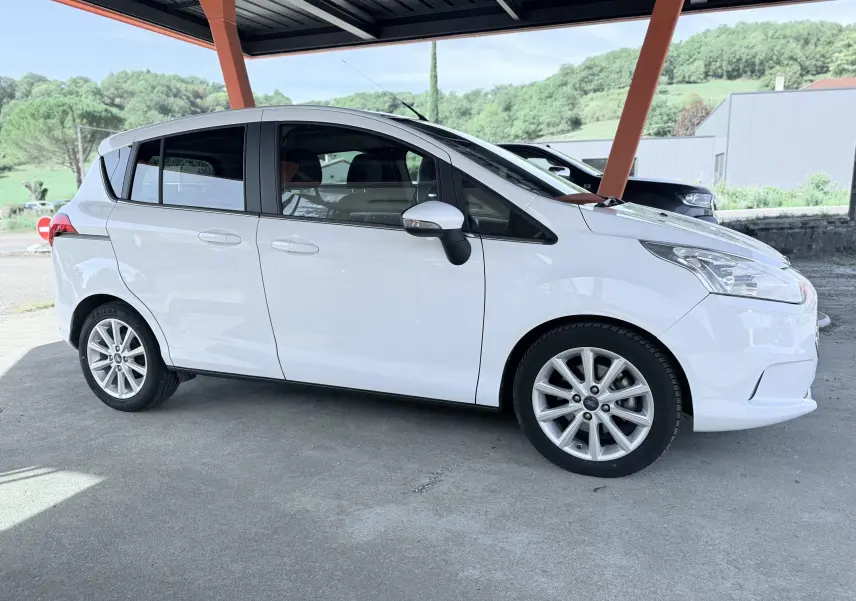 Vue de profil côté droit d'une Ford B-MAX blanche 2017 stationnée sous abri avec jantes alliage visibles.