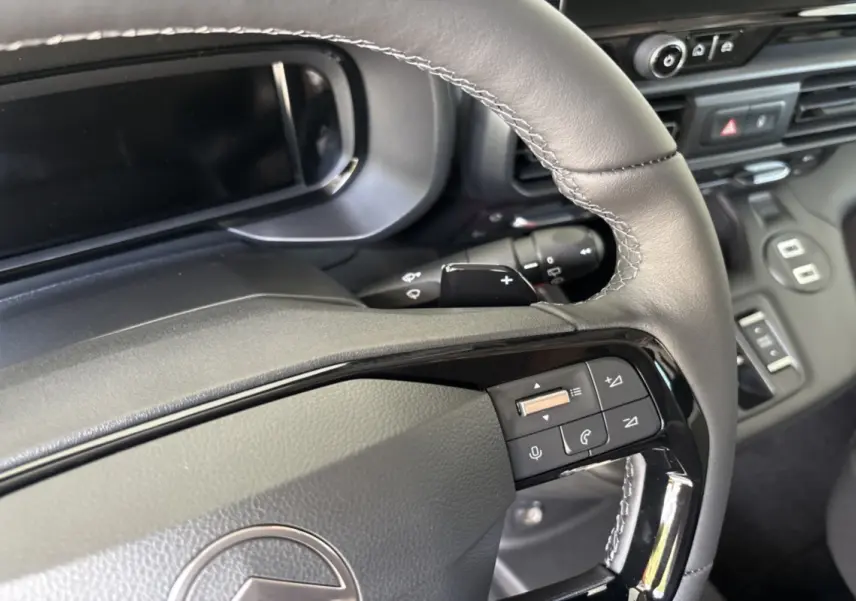 Gros plan sur le volant cuir multifonctions du Citroën Berlingo 2026, avec commandes intégrées et tableau de bord noir.