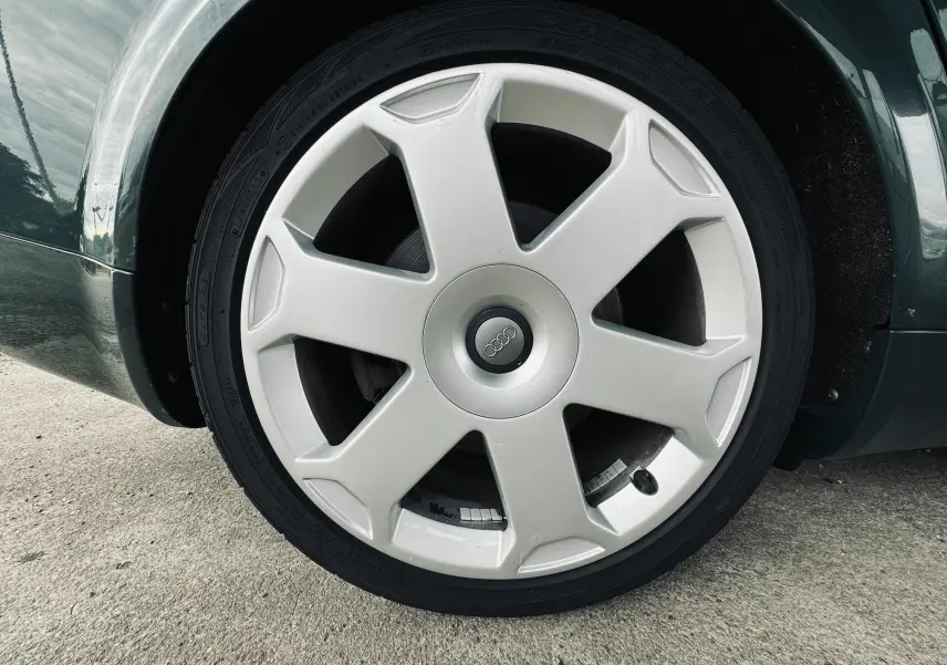 Gros plan sur la roue avant droite argentée d'une Audi S4 Avant verte de 2004, avec jante à 5 branches épaisses.
