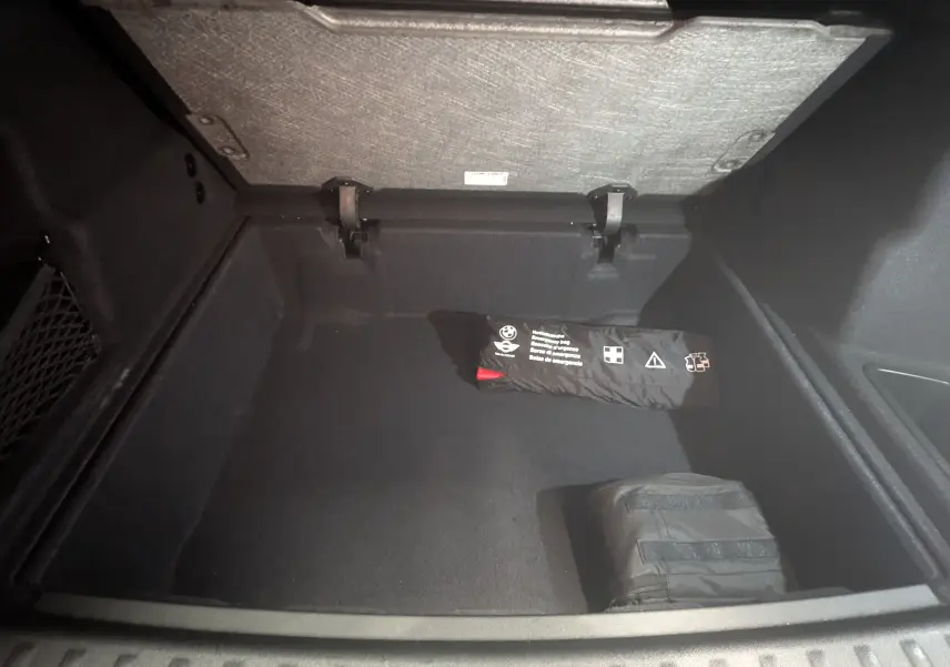 Vue intérieure du coffre noir d'un BMW X1 2025, avec trousse de secours et rangement sous plancher.