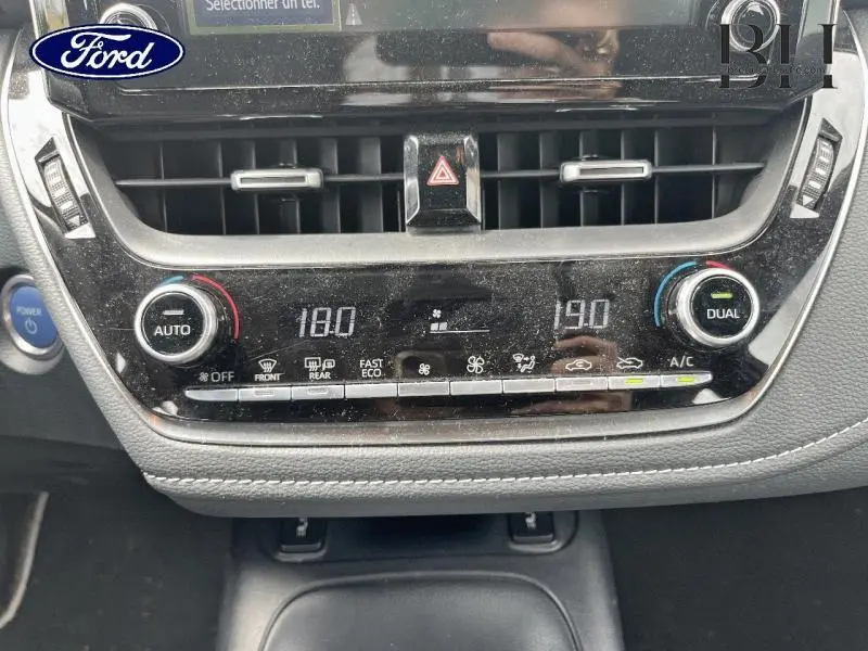 Vue rapprochée de la console centrale de la Toyota Corolla blanche, affichant la climatisation bi-zone et les commandes tactiles.