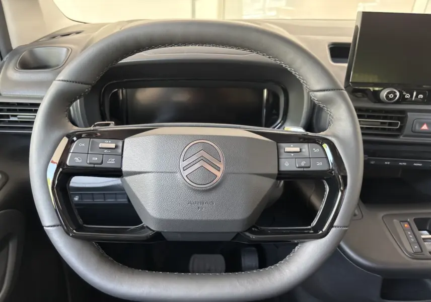 Vue rapprochée du volant cuir multifonctions noir du Citroën Berlingo 2026 avec tableau de bord et écran tactile en arrière-plan.