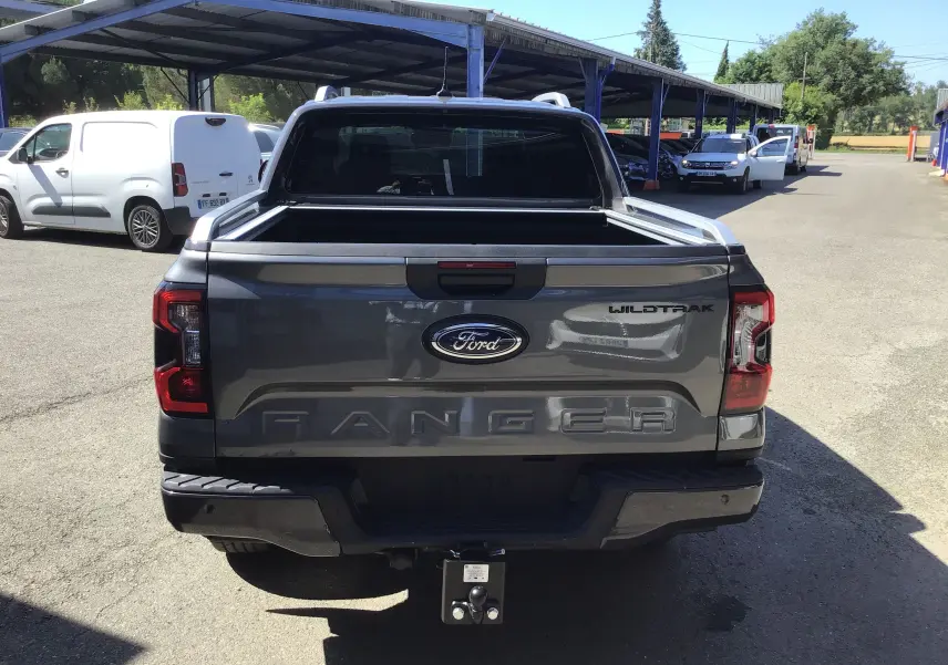 Vue arrière d'un Ford Ranger Wildtrak gris carbone avec plateau ouvert et attelage visible en extérieur.