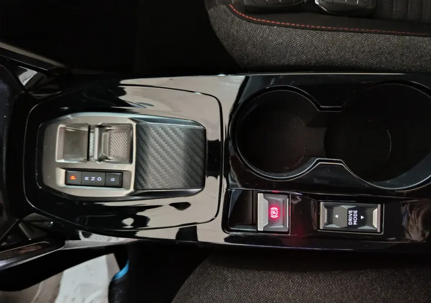 Gros plan sur la console centrale noire brillante de la Peugeot 208 électrique avec sélecteur de vitesse et frein à main électrique.