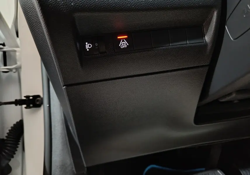 Gros plan sur les commandes d'assistance et réglage des phares côté gauche du tableau de bord noir d'une Peugeot 208 blanche électrique 2023.