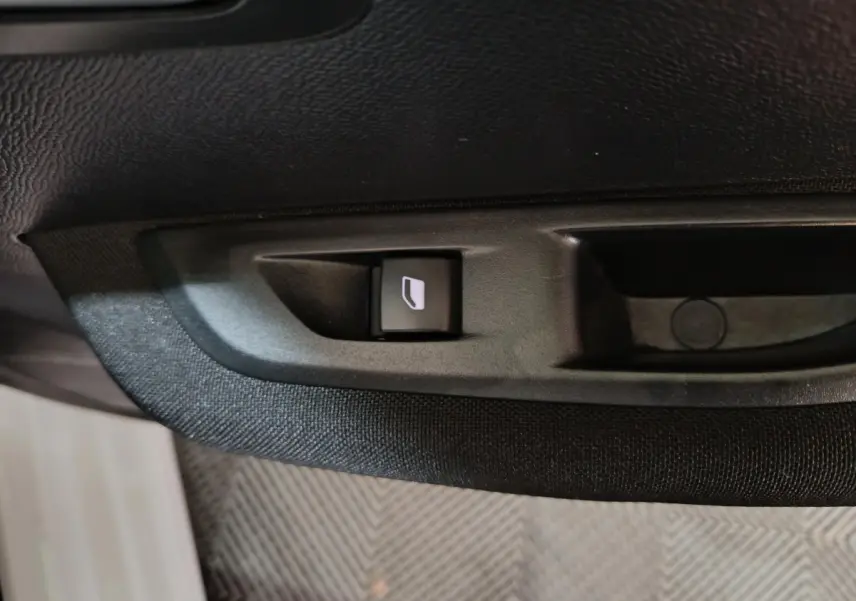 Bouton de commande de lève-vitre électrique sur la porte intérieure noire d'une Peugeot 208 électrique blanche.
