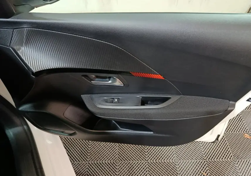 Vue rapprochée de la porte côté gauche d'une Peugeot 208 électrique blanche avec insert décoratif noir et rouge.