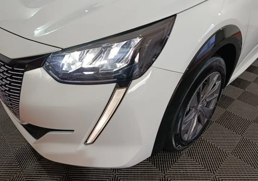 Gros plan sur l'avant droit blanc du Peugeot 208 électrique 2023, mettant en valeur le phare LED et la roue.