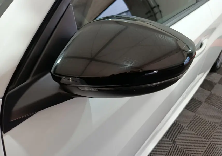 Rétroviseur noir côté gauche d'une Peugeot 208 électrique blanche vue en gros plan sur fond intérieur.