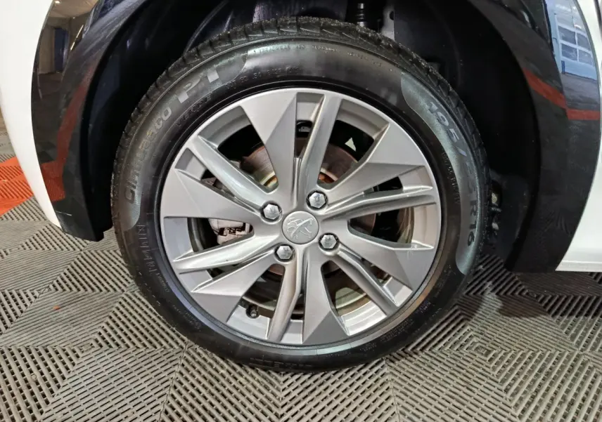 Gros plan sur la roue avant droite d'une Peugeot 208 électrique blanche, avec jante alliage argentée et logo lion central.