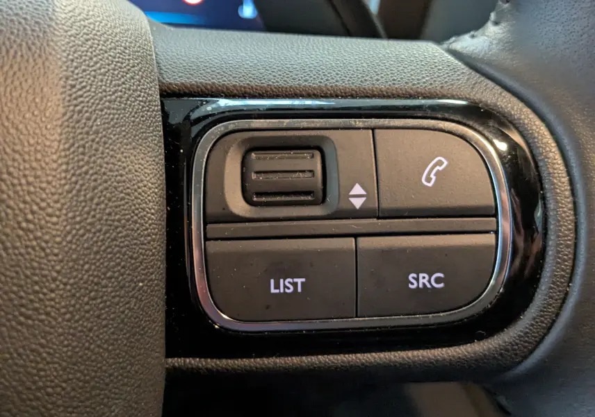 Gros plan sur les commandes du volant noir du Citroën C5 Aircross hybride 2025, boutons LIST et SRC visibles.