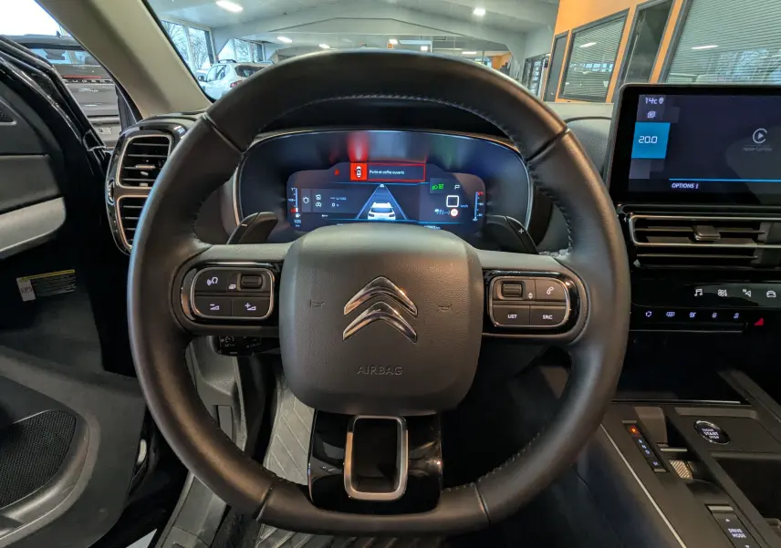 Vue intérieure centrée sur le volant cuir noir du Citroën C5 Aircross hybride 2025 avec tableau de bord digital et écran tactile.