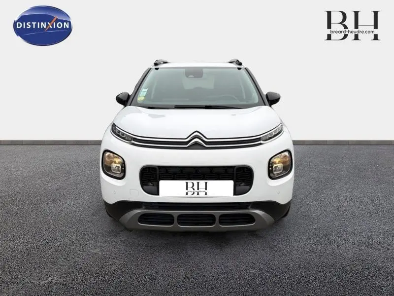 Vue avant d'un Citroën C3 Aircross blanc Natural White avec calandre noire et barres de toit visibles.
