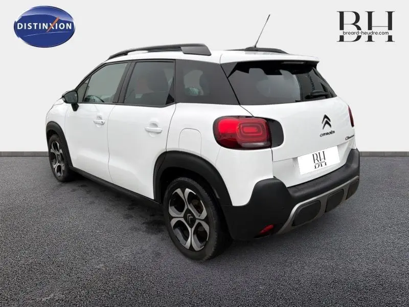 Vue 3/4 arrière droite d'une Citroën C3 Aircross blanche avec barres de toit noires et jantes diamantées.