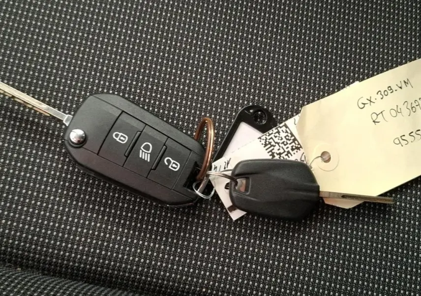 Gros plan sur clé de voiture Citroën C3 posée sur tissu gris à motifs, sans vue du véhicule.