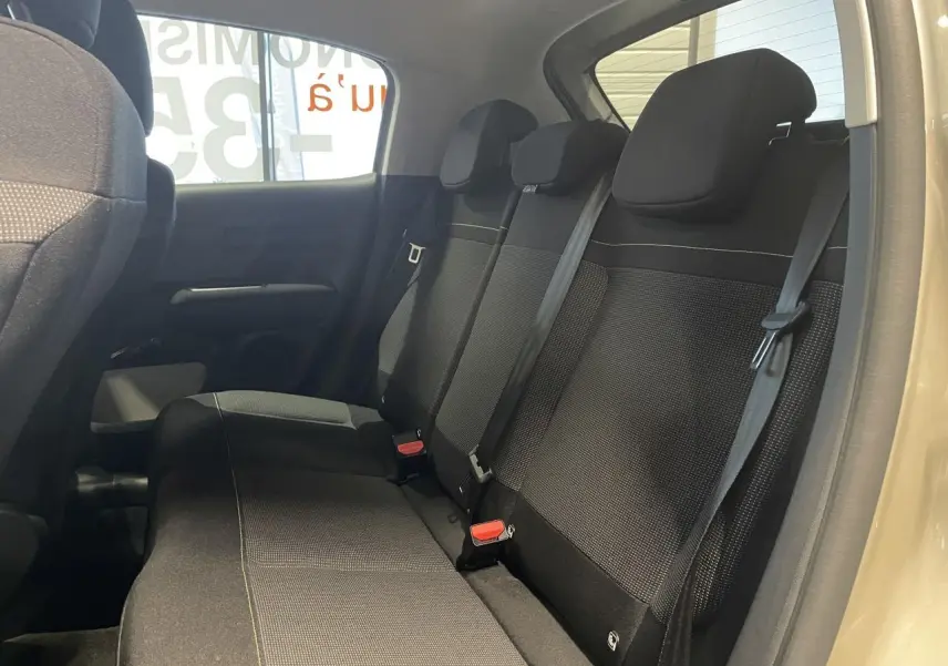 Vue intérieure côté droit sur la banquette arrière noire de la Citroën C3 beige clair 2024 avec ceintures de sécurité visibles.