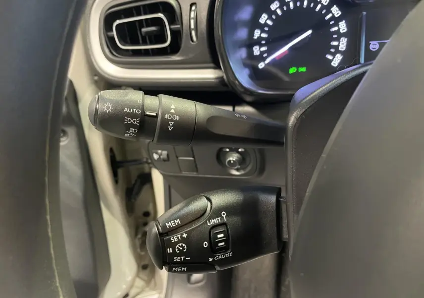 Gros plan sur les commandes au volant d'une Citroën C3 beige clair, avec tableau de bord et compteurs numériques visibles.