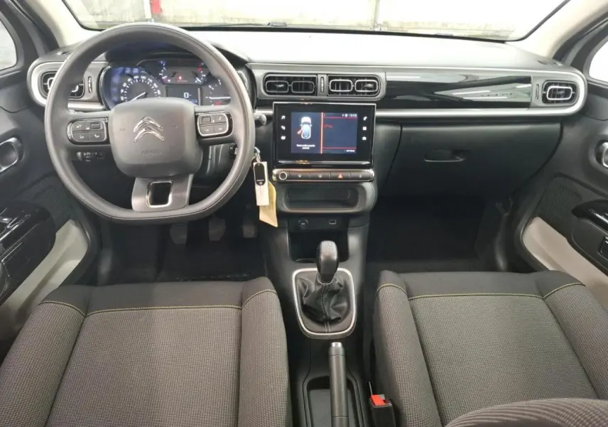 Intérieur avant du Citroën C3 2024, vue du conducteur, tableau de bord noir brillant et sièges tissu gris avec surpiqûres jaunes.