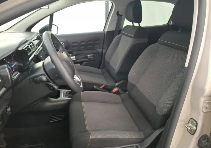 Vue intérieure côté conducteur de la Citroën C3 beige clair 2024, sièges tissu gris avec surpiqûres jaunes.