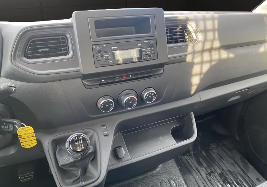 Vue intérieure du tableau de bord noir du Renault Master 2024, avec levier de vitesses manuel et commandes climatisation visibles.