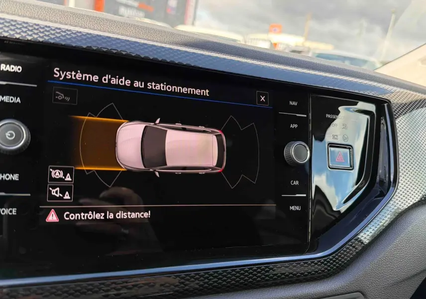 Écran tactile intérieur montrant le système d'aide au stationnement de la Volkswagen Polo blanche, vue de face.