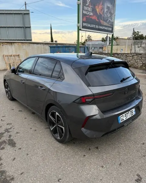 Opel Astra 1.5 Diesel gris vue 3/4 arrière droit, avec feux arrière fins et jantes noires distinctives.