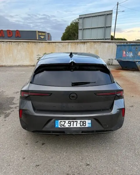 Vue arrière d'une Opel Astra gris foncé 2024 avec vitres teintées et feux arrière étirés, stationnée sur un parking extérieur.
