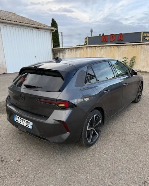 Vue 3/4 arrière droite d'une Opel Astra 2024 gris métallisé avec feux arrière effilés et jantes alliage noires.
