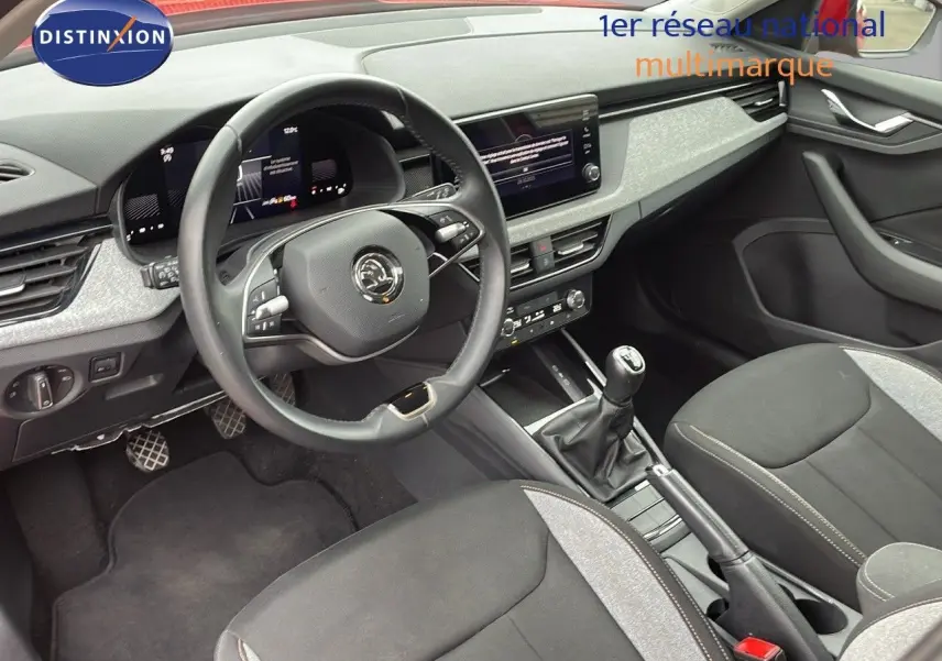 Vue intérieure avant du Skoda Kamiq 2024, montrant le volant, la console centrale avec boîte manuelle et les sièges tissu gris noir.