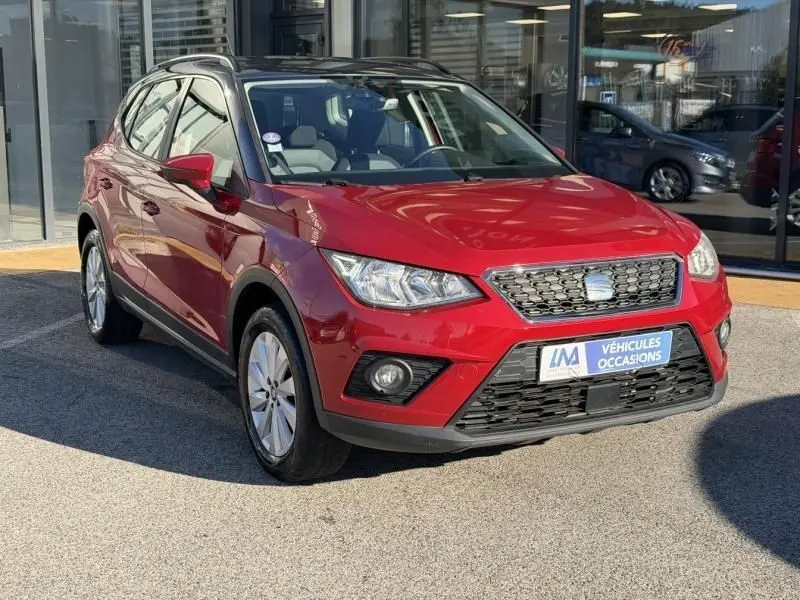 SEAT Arona rouge métal vue 3/4 avant droit, avec calandre noire et jantes alliage, stationné devant un showroom.