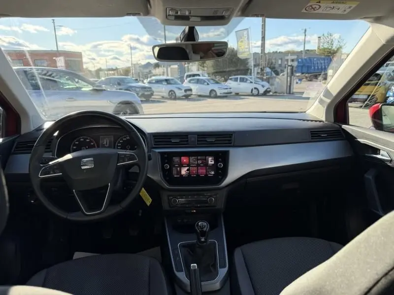Vue intérieure avant du SEAT Arona rouge métal 2019, montrant le tableau de bord avec écran tactile et levier de vitesses manuel.