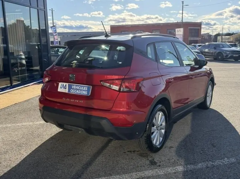 Vue 3/4 arrière droite d'une SEAT Arona rouge métal 2019, avec toit noir et détails noirs sur le bouclier arrière.