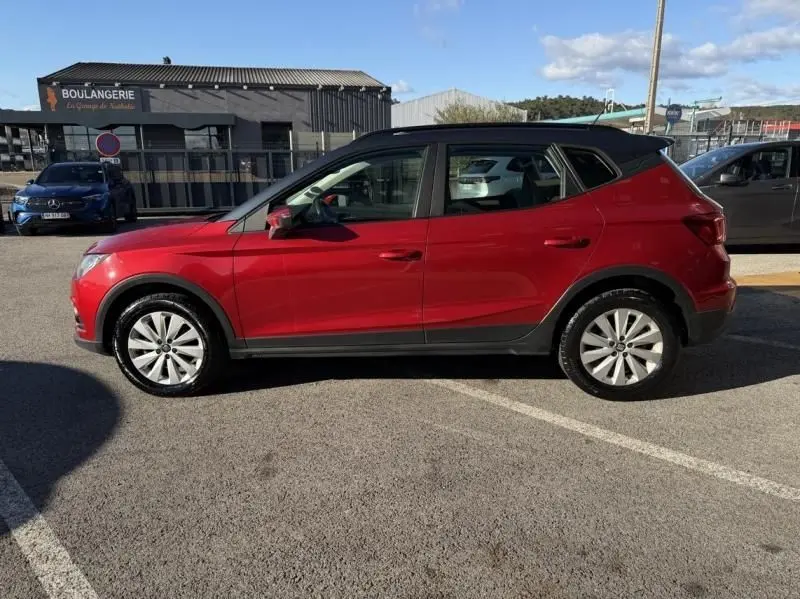 Vue de profil côté gauche d'un SEAT Arona 1.0 TSI 95 STYLE rouge métal, compact et moderne, stationné en extérieur.
