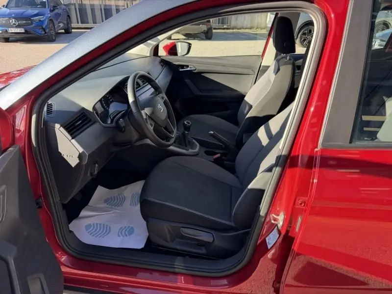Vue intérieure côté conducteur d'une SEAT Arona rouge métal 2019, mettant en valeur les sièges noirs et la boîte manuelle.