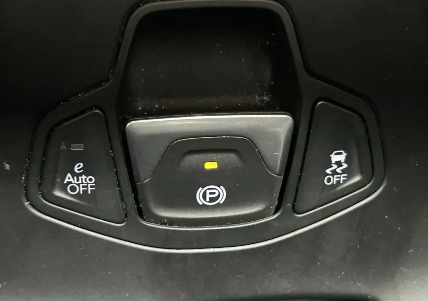 Gros plan sur les boutons de commande du frein à main électronique et des aides à la conduite dans une Jeep Renegade gris graphite.