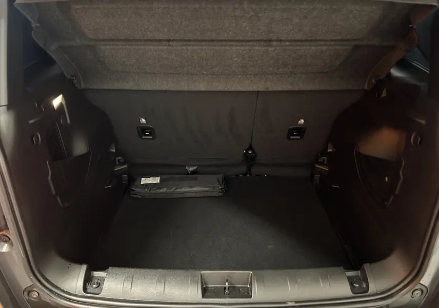 Coffre ouvert de Jeep Renegade gris graphite, vue arrière montrant l’espace de rangement et un kit plié au sol.