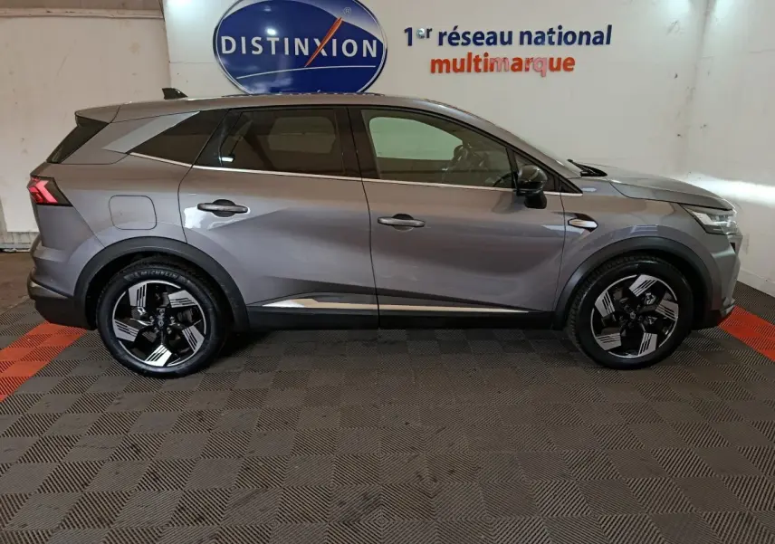 Vue de profil côté gauche d’un Renault SYMBIOZ gris avec jantes noires et détails chromés, en intérieur showroom.
